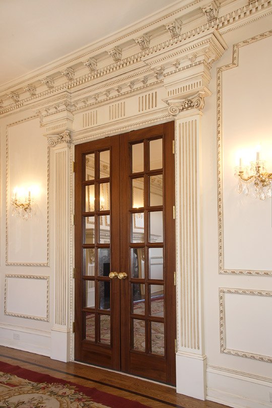 Panelled hallway with mahogany French doors and wall sconces in an Alliotts home